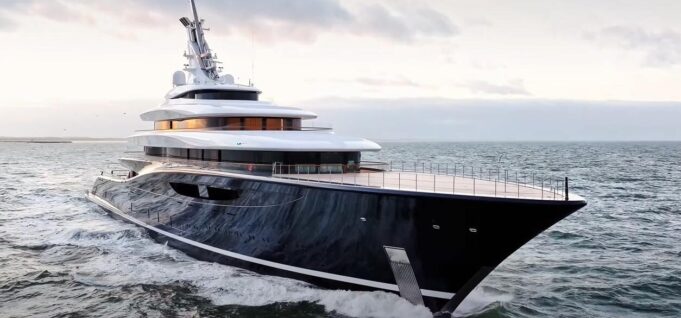 Large luxury motor yacht with a dark hull cruises the open sea at sunset, multi-deck white superstructure visible.