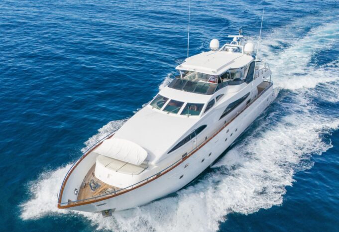 White luxury motor yacht cruising through deep blue ocean, creating a frothy wake.